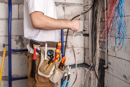 Electrician working near the Board with wires. Installation and connection of electrics. Professional with tools in hand.